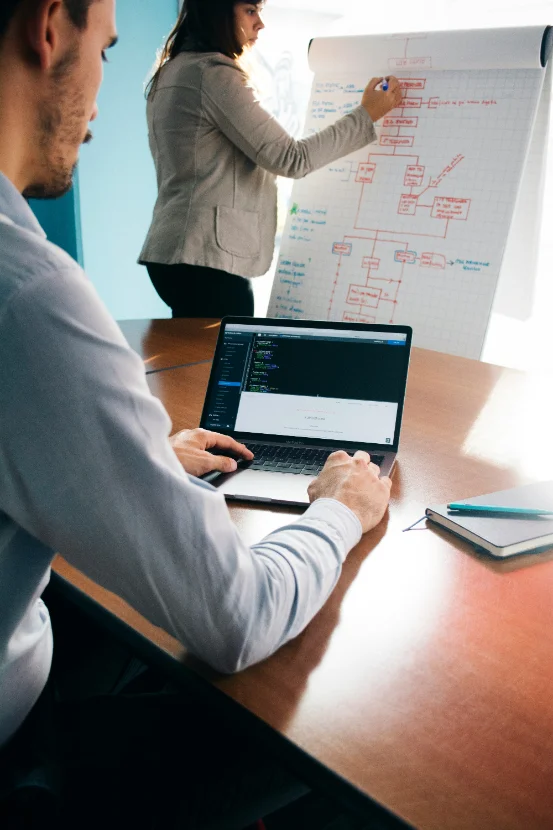 Two colleagues mapping a system on a whiteboard beside a laptop